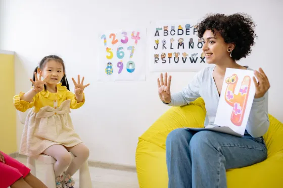 A young girl counting on her fingers with a smiling teacher