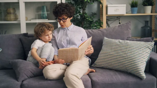 A parent reading a book with a young child on the couch